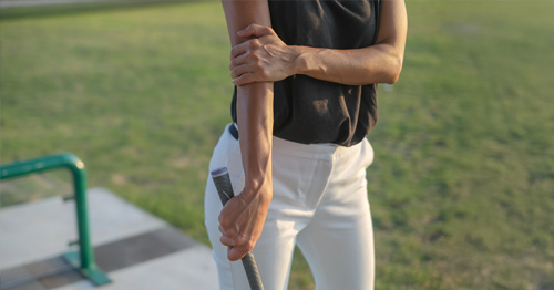 A woman with a golf club holding her elbow in pain.